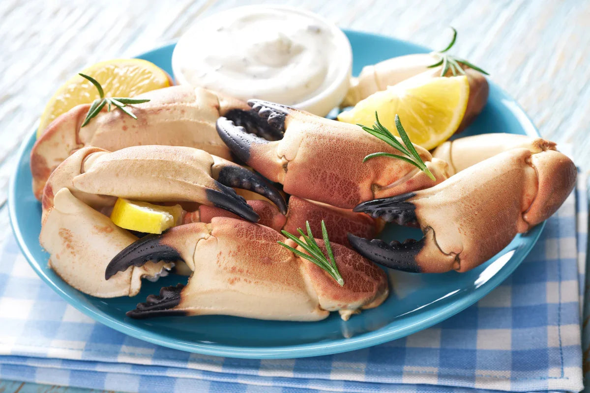 Fresh cooked crab claws on a blue plate with lemon wedges, herbs, and seafood sauce