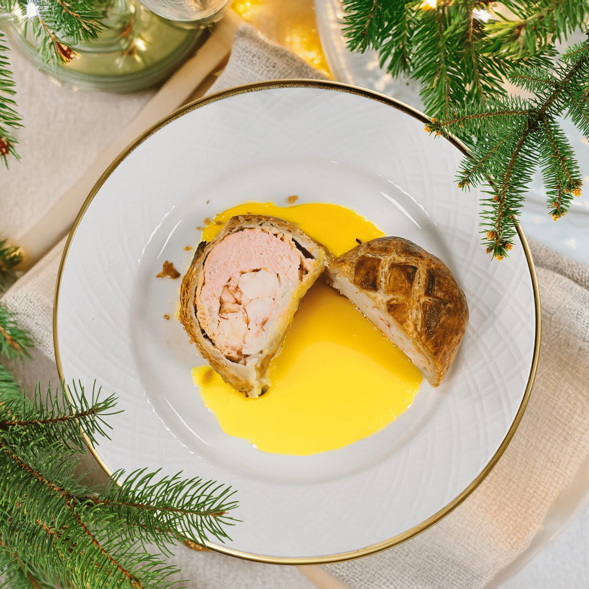 Lobster Wellington sliced on a plate with golden sauce, festive table setting