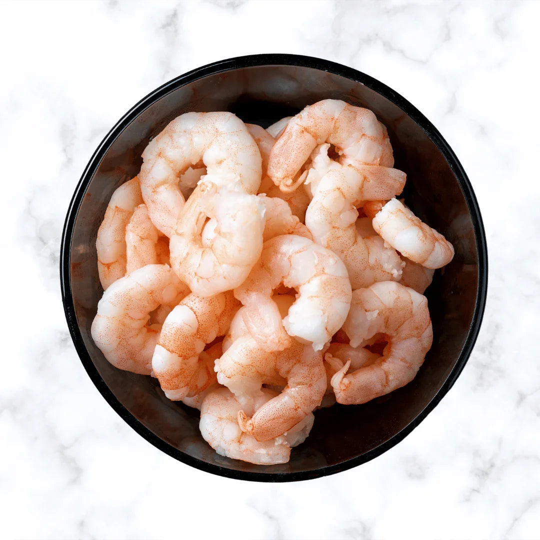 Cooked peeled prawns in a black bowl on a marble background, fresh seafood