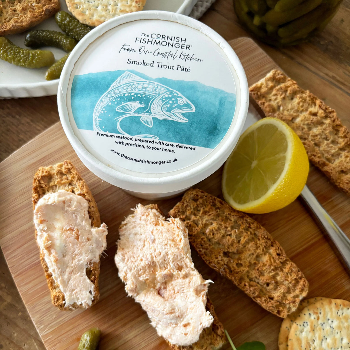 Smoked trout pâté with crispbread, lemon, and pickles on a wooden board