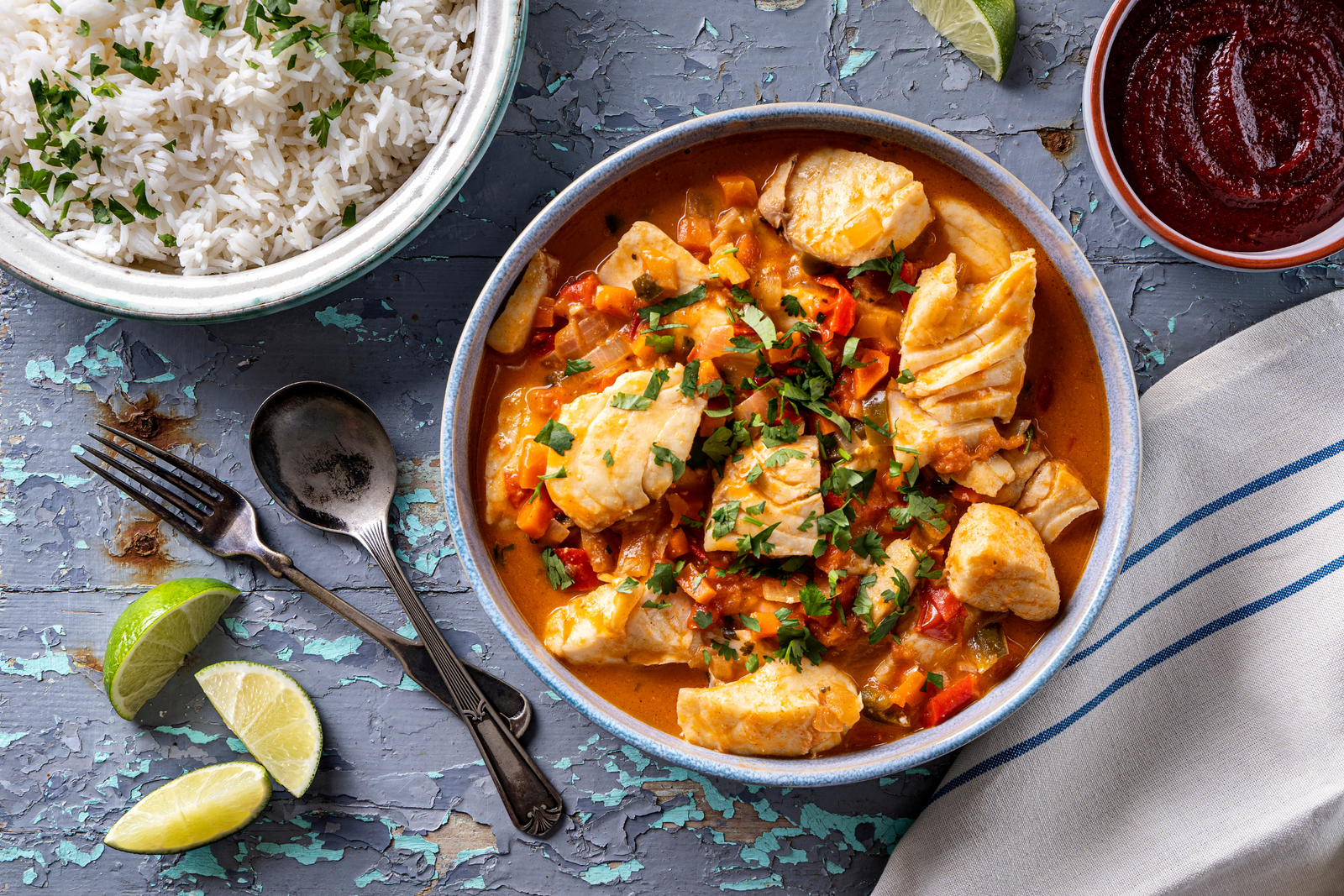 Bowl of BBQ cod and chorizo stew garnished with herbs, served with rice and lime wedges