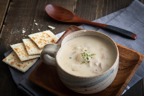 Creamy monkfish and clam chowder in a rustic bowl with crackers and a wooden spoon