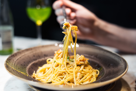 Crab linguine pasta with chilli and parsley served in a brown bowl, hand twirling forkful