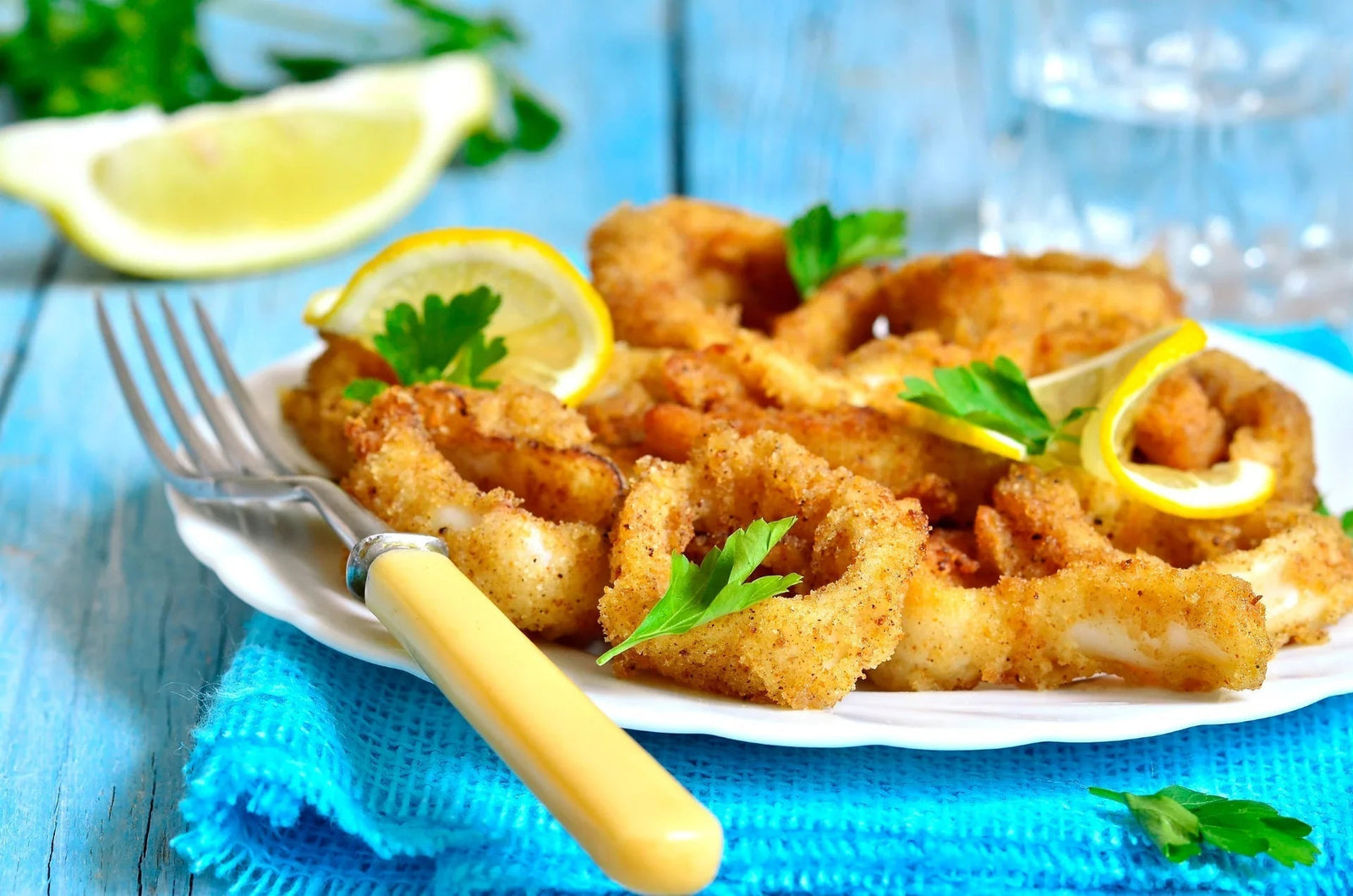 Crispy calamari rings with lemon slices and parsley on a white plate, seafood dish