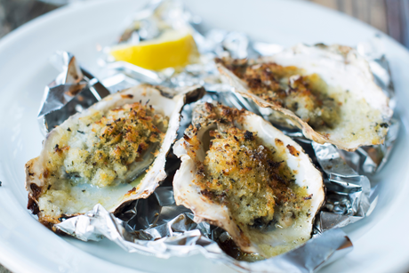 Baked oysters topped with garlic herb gratin and breadcrumbs on foil, served with lemon wedge