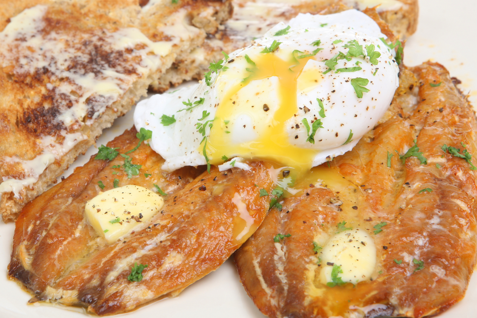Smoked kippers with poached egg, melted butter, parsley, and buttered toast on a plate