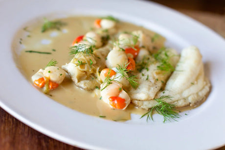 Cooked lemon sole and scallops in a creamy sauce, garnished with fresh herbs on a white plate
