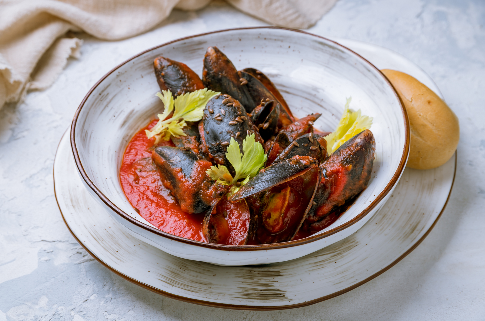 Mussels in spicy tomato sauce garnished with celery and served with a bread roll