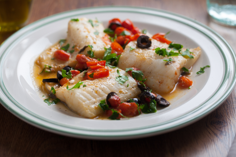 Mediterranean plaice fillets with tomatoes, olives, and herbs on a white plate