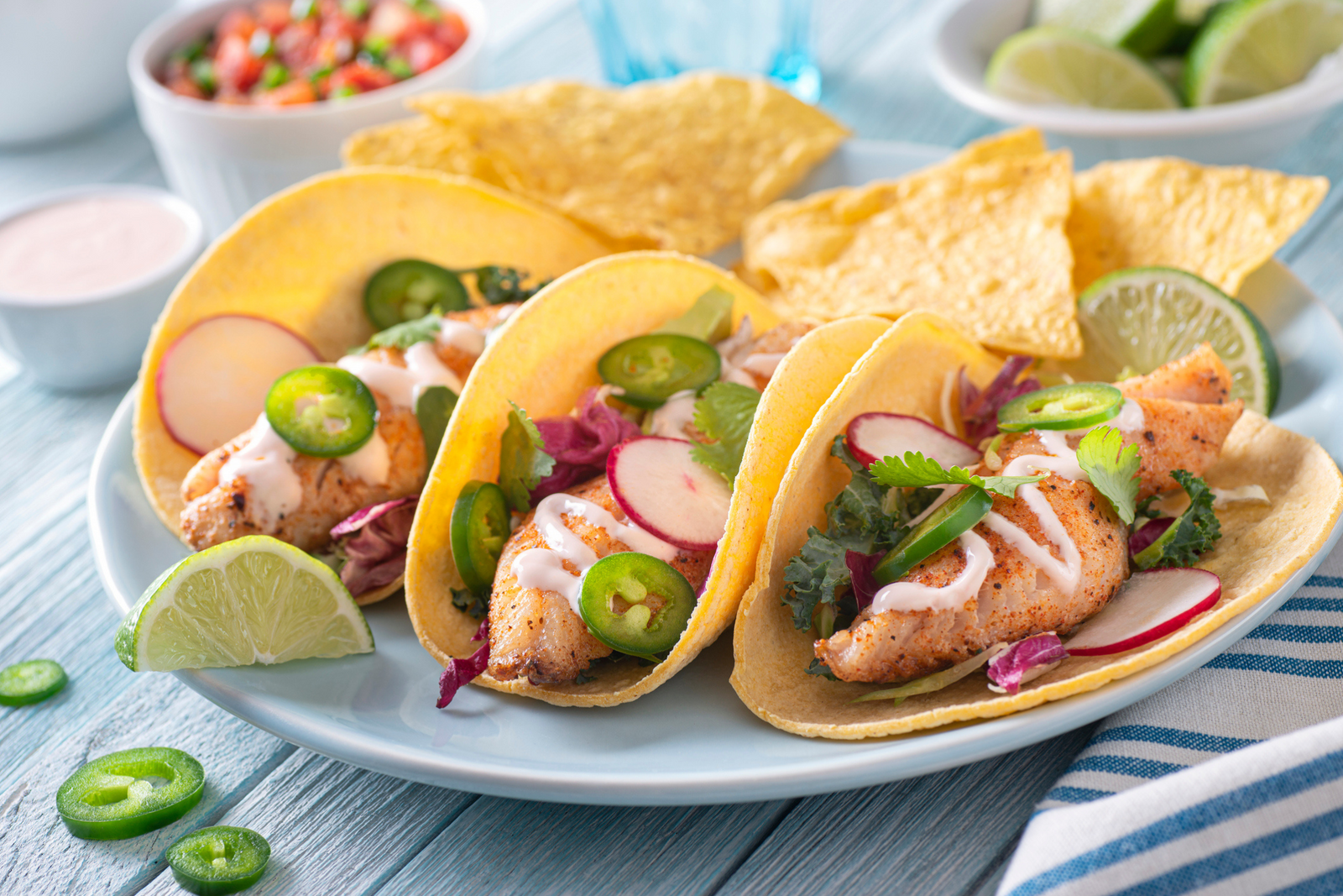 Grilled monkfish tacos with fresh vegetables, lime wedges, and tortilla chips on a plate
