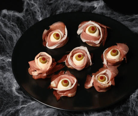 Halloween-themed smoked fish and cream cheese bites shaped like eyes, garnished with olives on a black plate