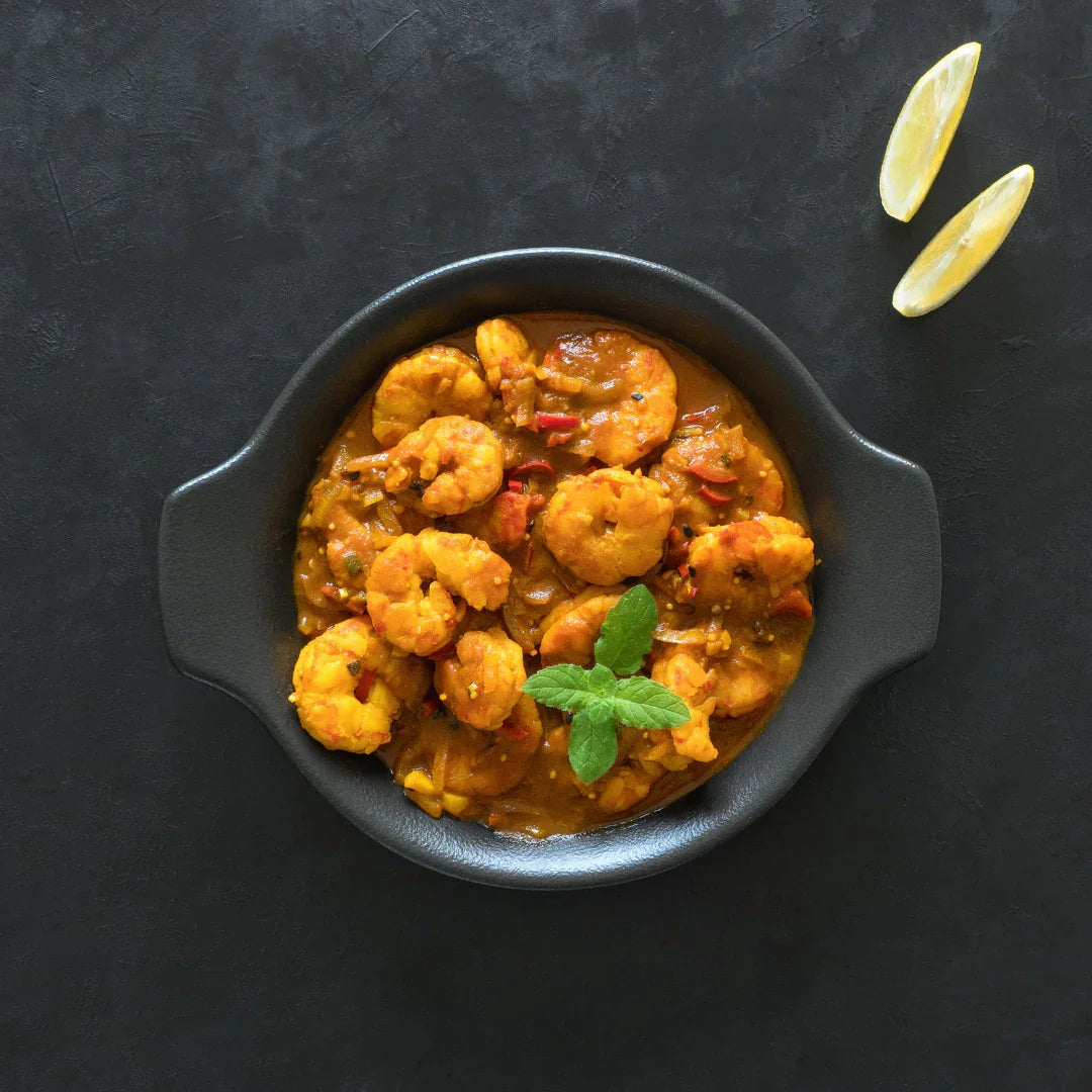 Prawn and chickpea curry in a black bowl with fresh herbs and lemon wedges on a dark background