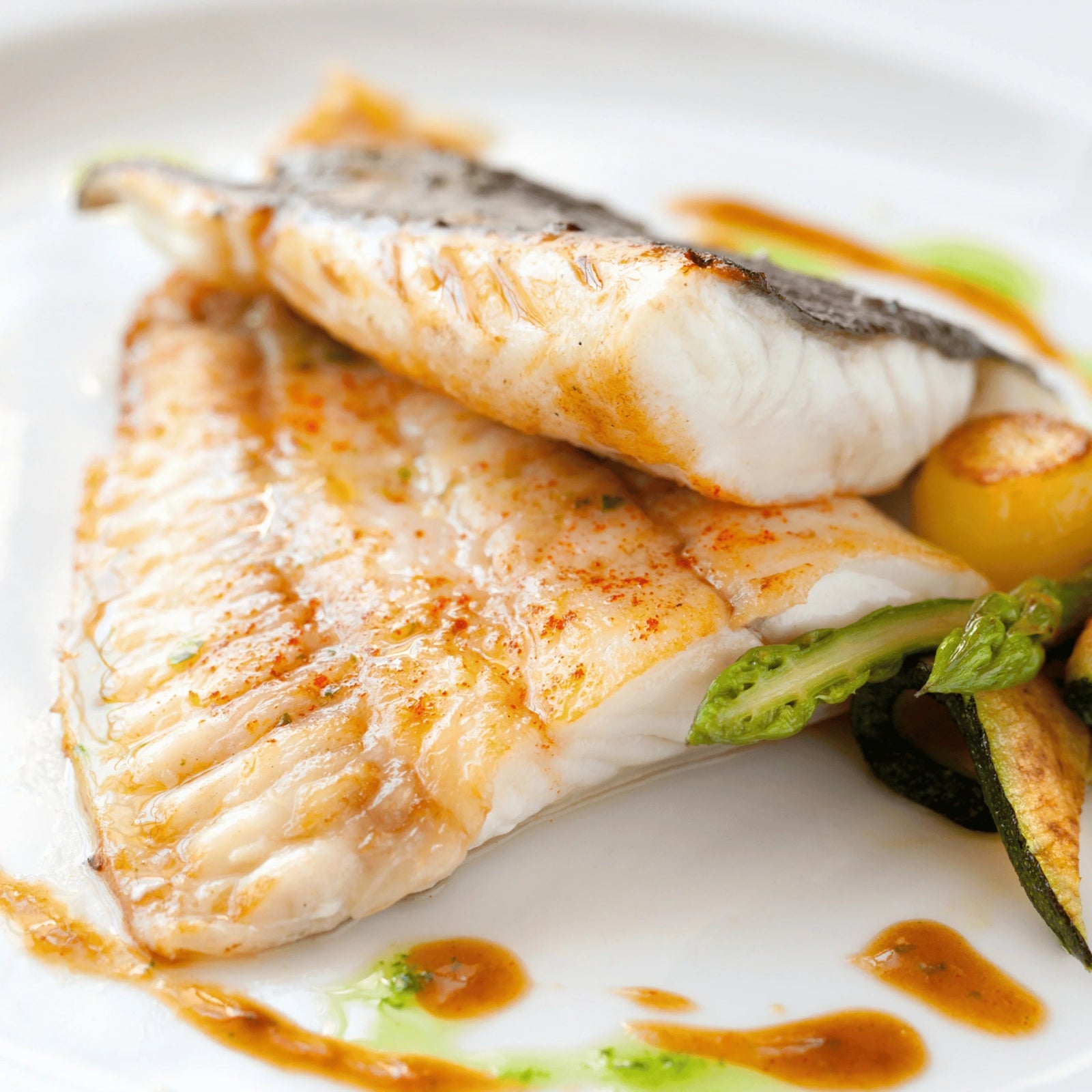 Roast turbot fillet with fennel, fresh vegetables and sauce on a white plate