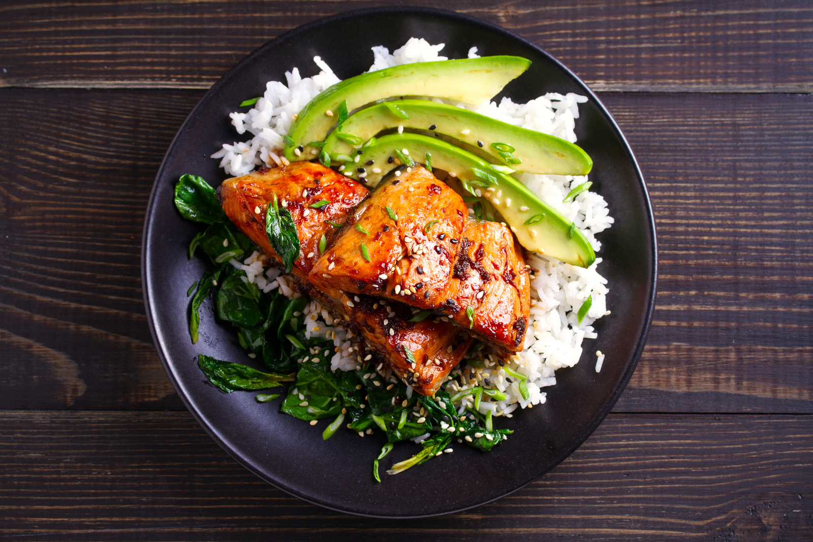 Roasted honey soy salmon served on rice with avocado and sauteed spinach, garnished with sesame seeds