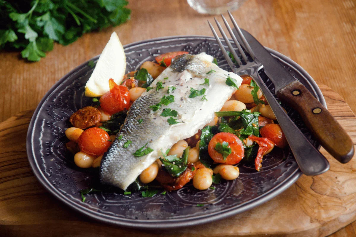 Sea bass fillet with chorizo, butter beans, cherry tomatoes, and fresh herbs on a plate