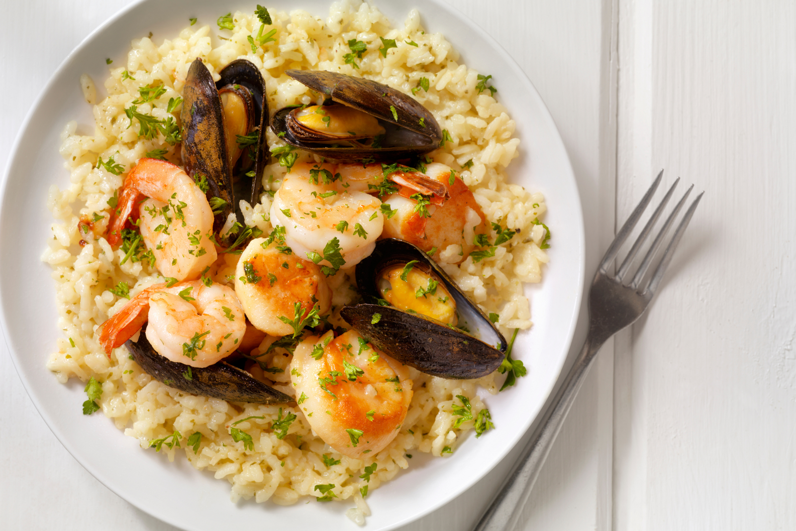 Seafood risotto with prawns, mussels, and scallops on white plate, garnished with herbs