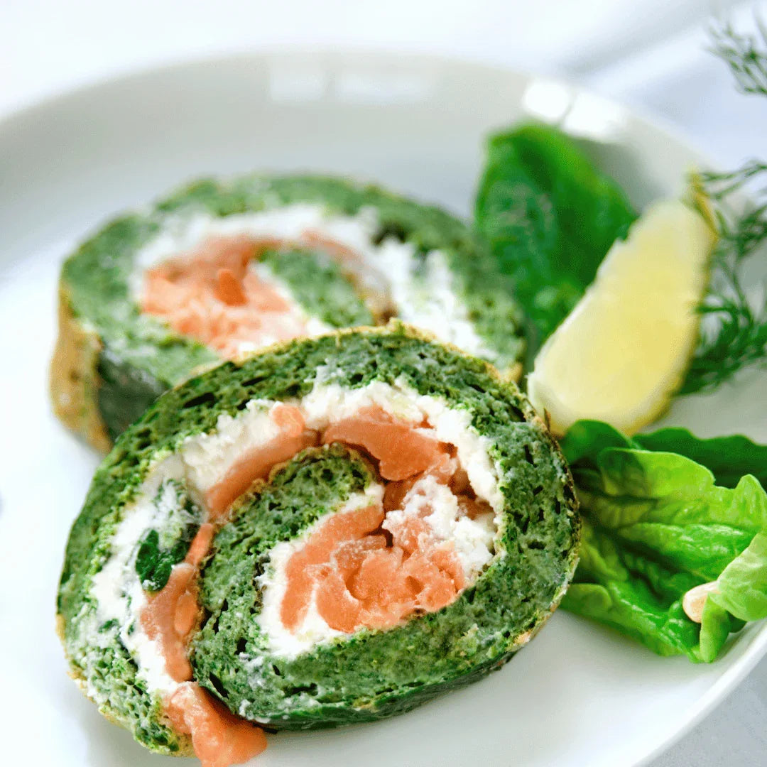 Spinach-wrapped smoked trout roulade with cream cheese, lettuce, lemon wedge, and dill on a plate