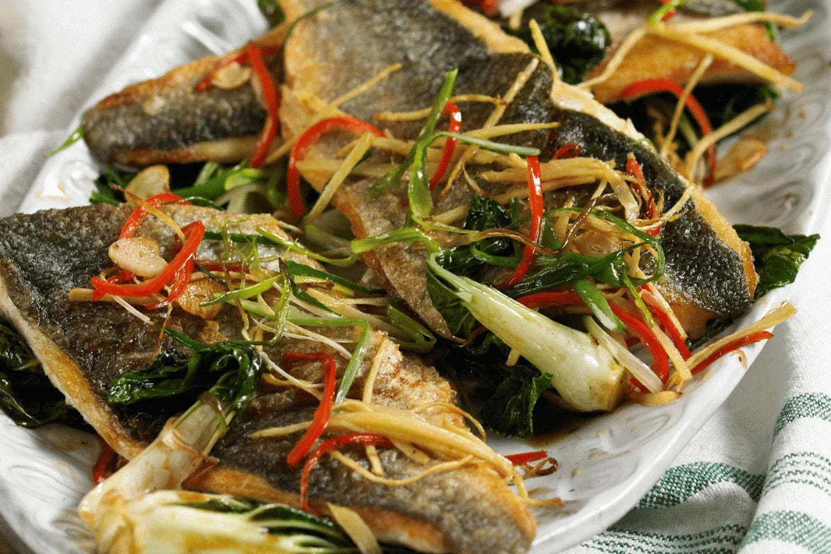 Sticky Asian sea bass fillets with spring onions, chili, ginger and greens on a platter