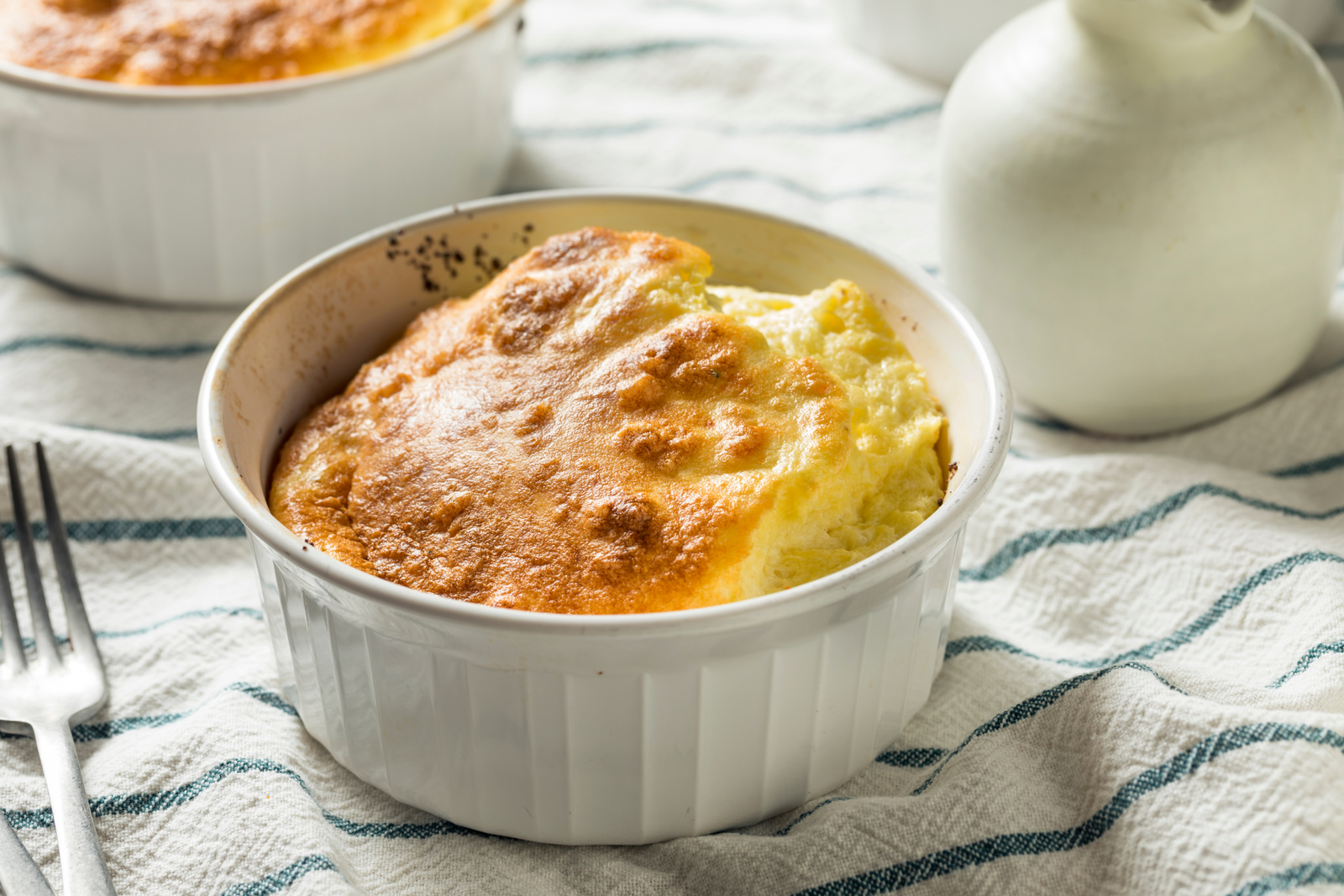 Golden twice baked crab soufflé in a white ramekin on a striped kitchen towel