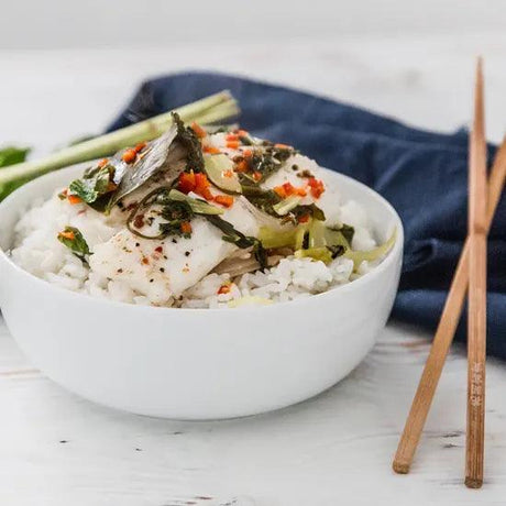 Bowl of steamed white fish with herbs and rice, garnished with vegetables and chopsticks