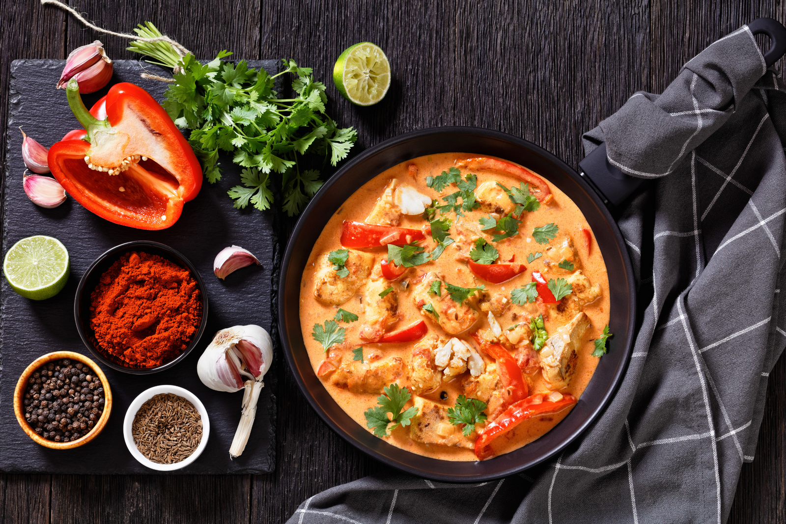 Thai red fish curry in a black bowl with red pepper, herbs, and spices on a rustic table