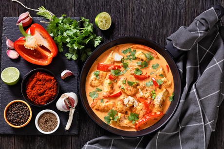 Thai red fish curry in a black bowl with red pepper, herbs, and spices on a rustic table