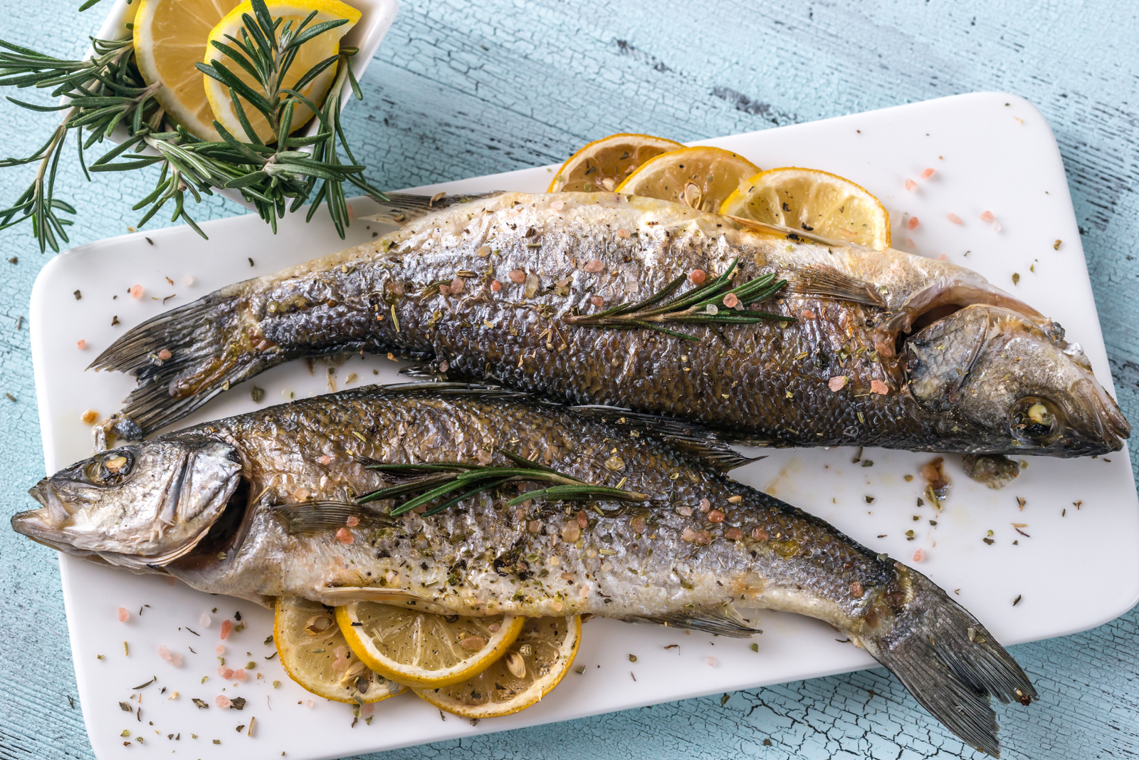 Whole baked sea bass with herbs and lemon slices on a white plate