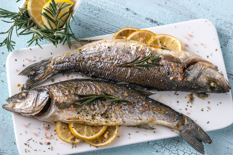 Whole baked sea bass with herbs and lemon slices on a white plate