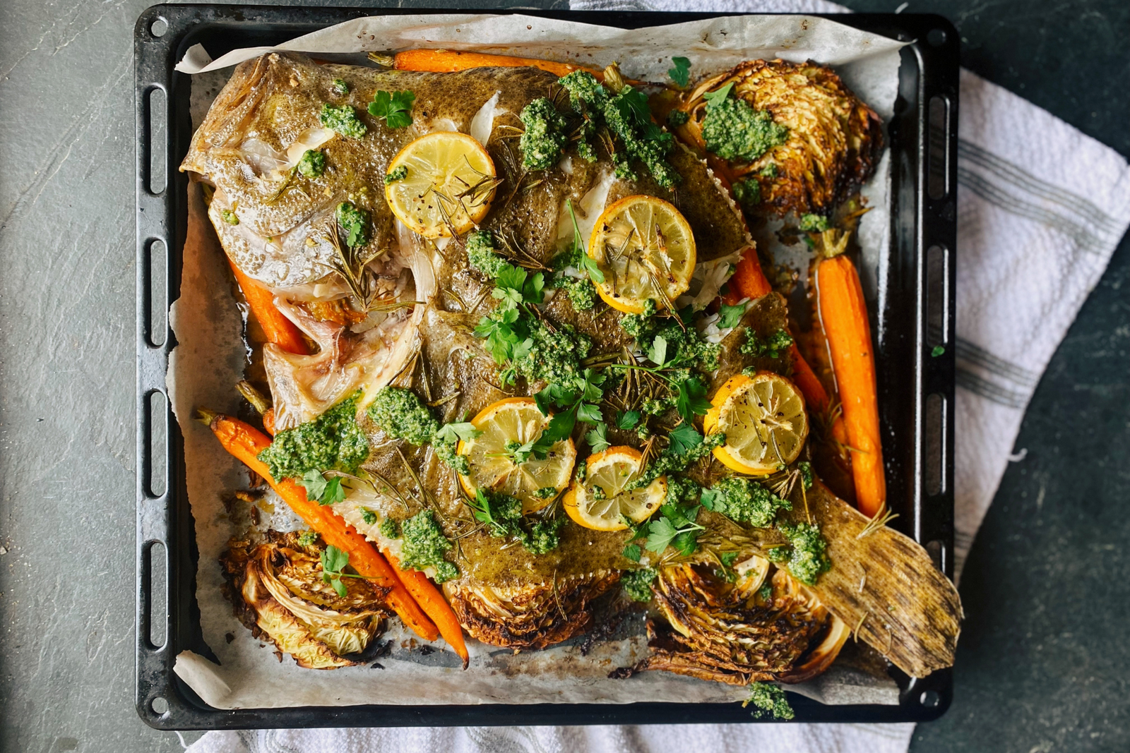 Whole roasted turbot with lemon slices, herbs, carrots, and cabbage on a baking tray