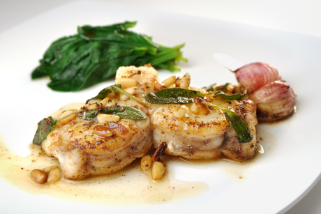 Whole roasted monkfish with pine nuts, sage, wilted greens, and roasted shallots on a white plate