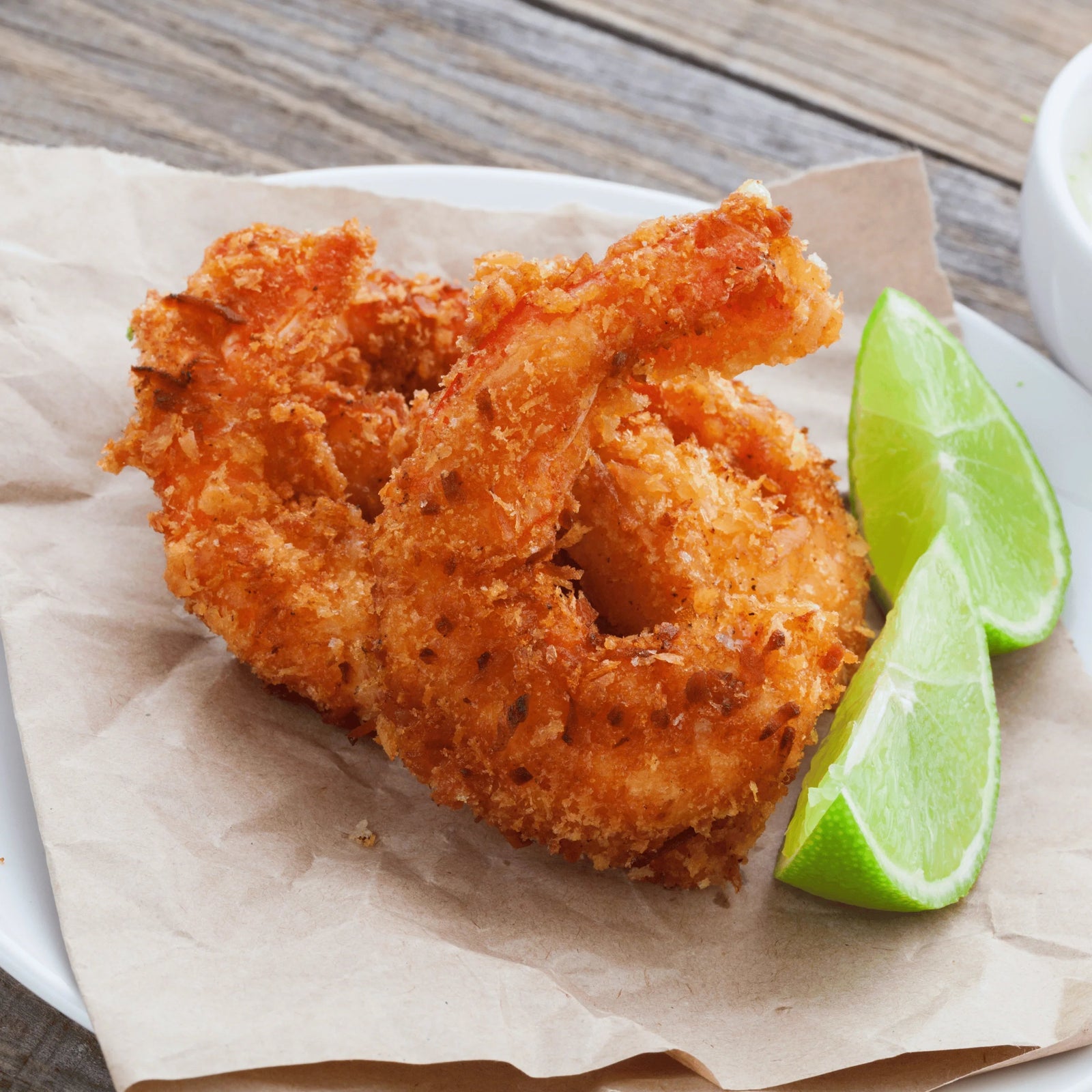 Crispy coconut prawns served on parchment with fresh lime wedges, seafood appetizer