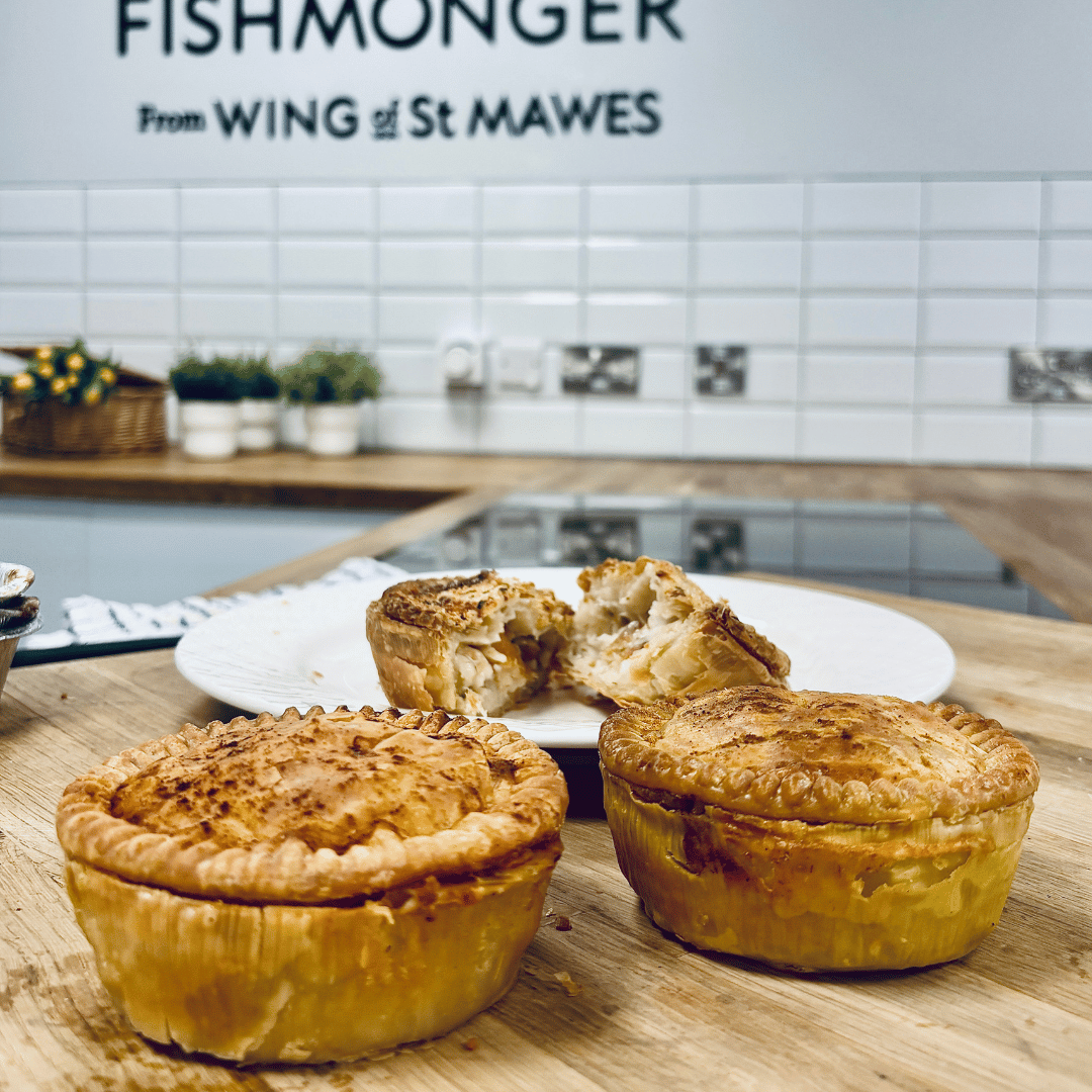 Assorted golden fish pies with flaky pastry on a kitchen counter, one pie cut open