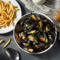 Bowl of Moules Marinière mussels in sauce with a side of golden French fries