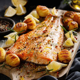 Roasted salmon fillet garnished with herbs, lemon wedges, and roasted potatoes on a wooden board