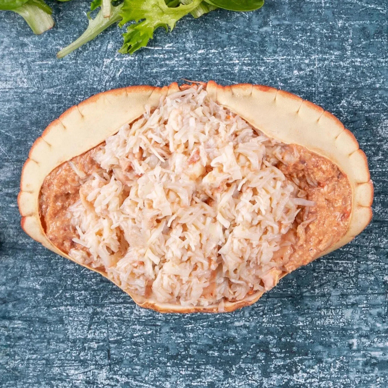 Dressed crab in shell with white and brown crab meat, served on rustic blue surface